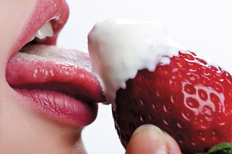 woman sensuously eating a strawberry with whip cream on it